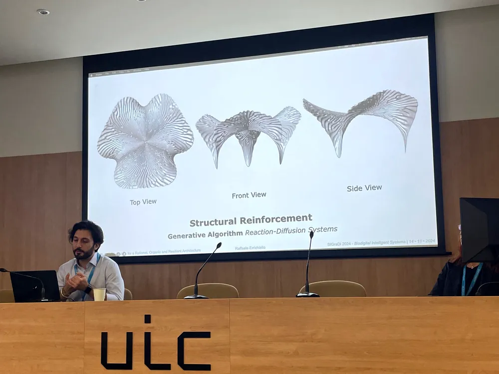 Raffaele at the speakers' table at UIC Barcelona, the slide behind him showing AURORA's reaction-diffusion reinforcement in top, front and side view