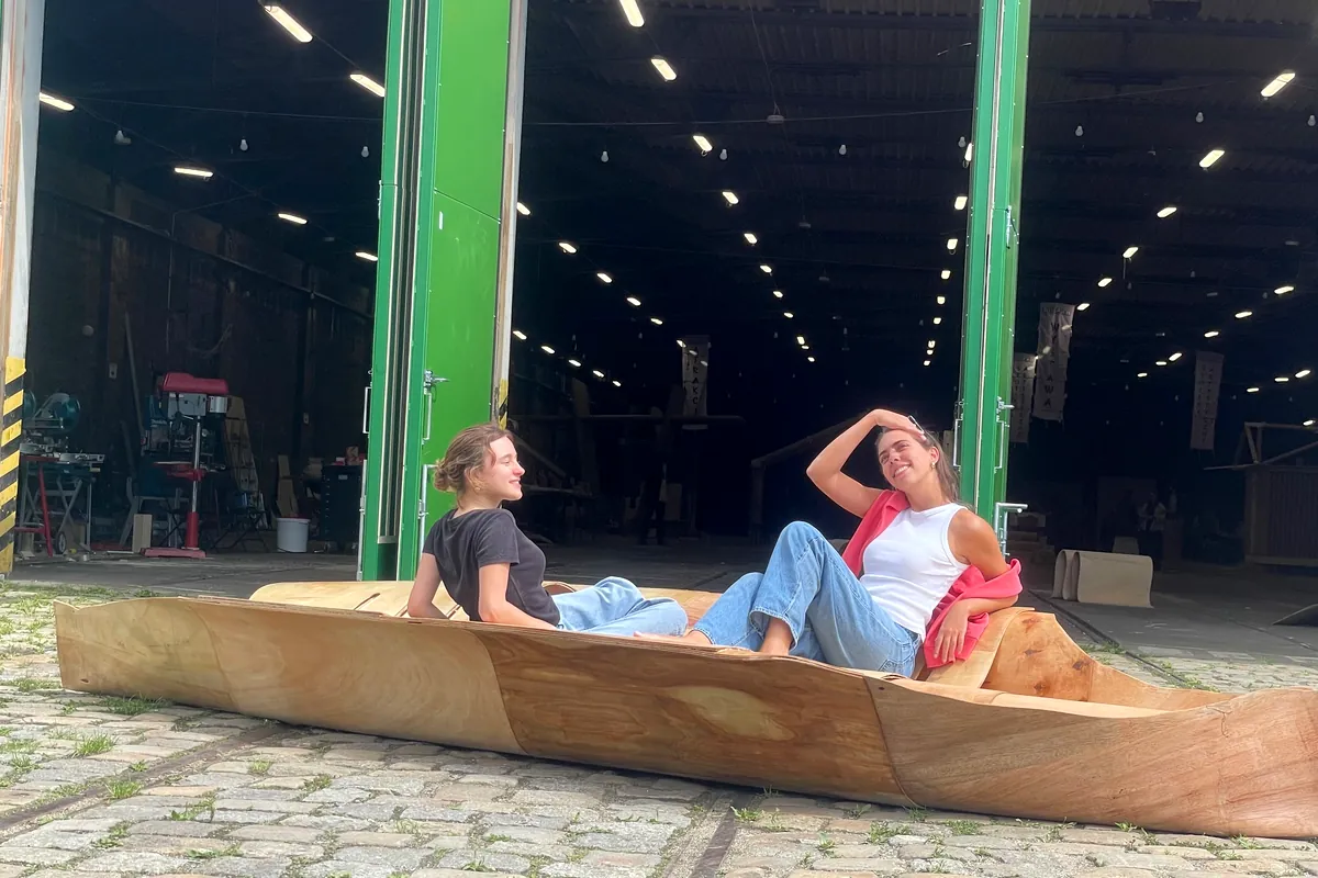 Two students lying in the finished canoe on the cobbles outside the hall