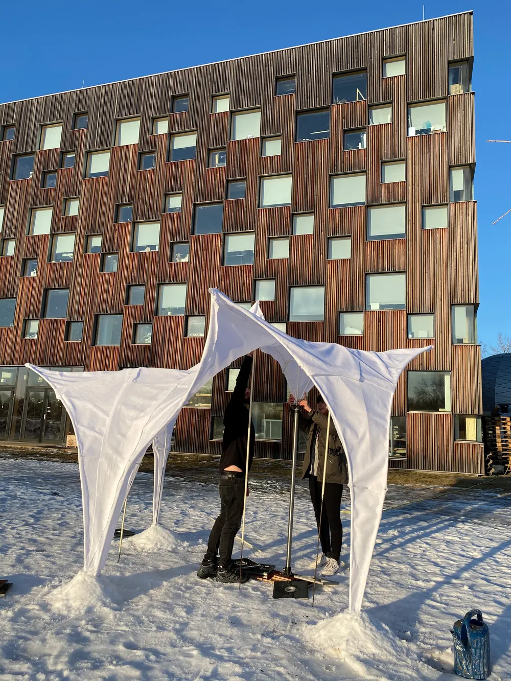 The prototype in front of the school's timber facade, two people adjusting the poles from behind