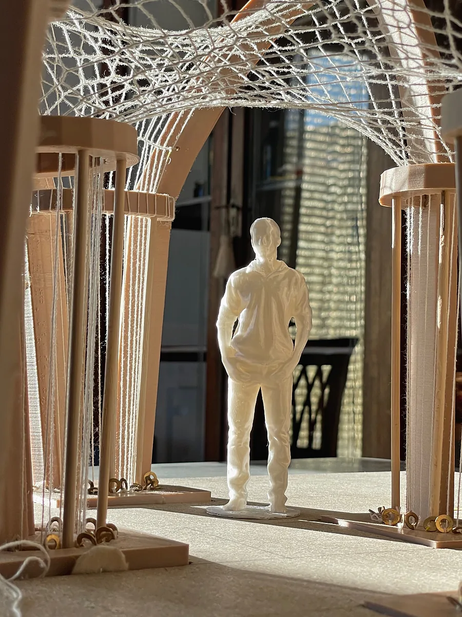 Model of arches cut from board carrying a net of white string, a small printed figure standing under it